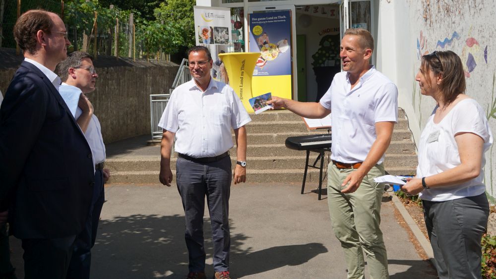 Vier Männer und eine Frau stehend auf einem Pausenhof im Gespräch