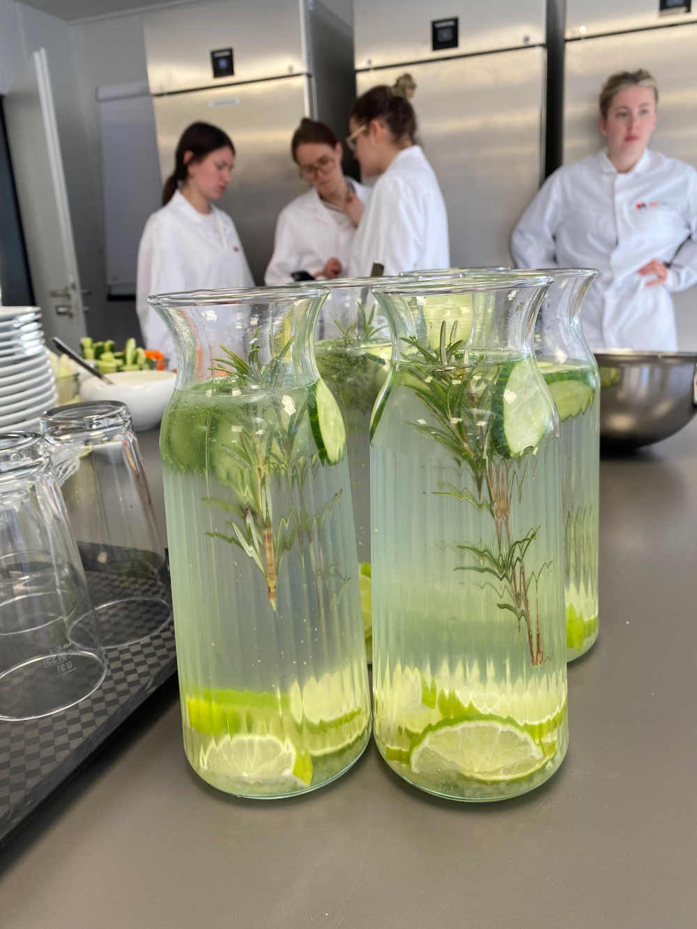 Karaffen mit Wasser, Limetten, Gurke und Rosmarin stehen auf einer Arbeitsplatte.