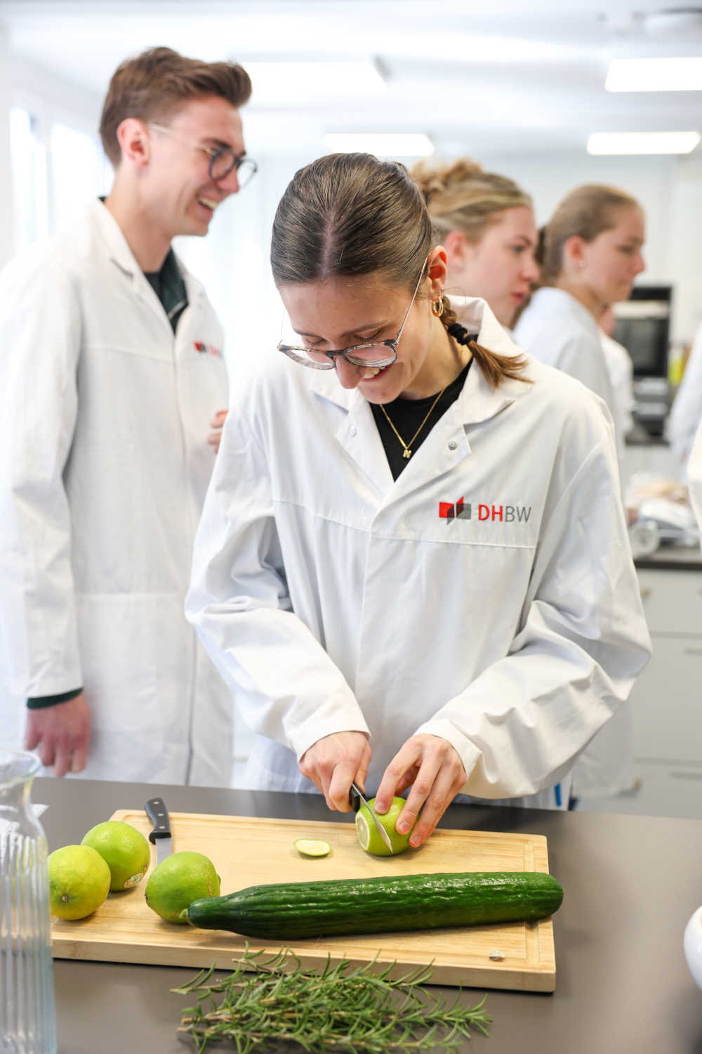 Eine junge Frau schneidet eine Limette auf einem Holzbrett. Sie trägt einen Schutzkittel der DHBW Heilbronn.