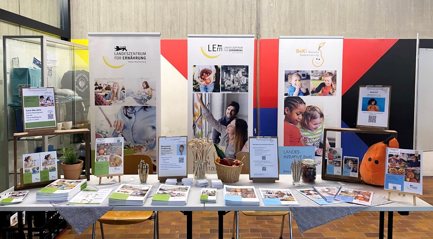 Infostand des LErn BW, im Vordergrund 2 Tische mit verschiedenen Bildungsmaterialien zur Ernährungsbildung und Gemeinschaftsverpflegung, im Hintergrund Banner des LErn BW und der Landesinititative BeKi
