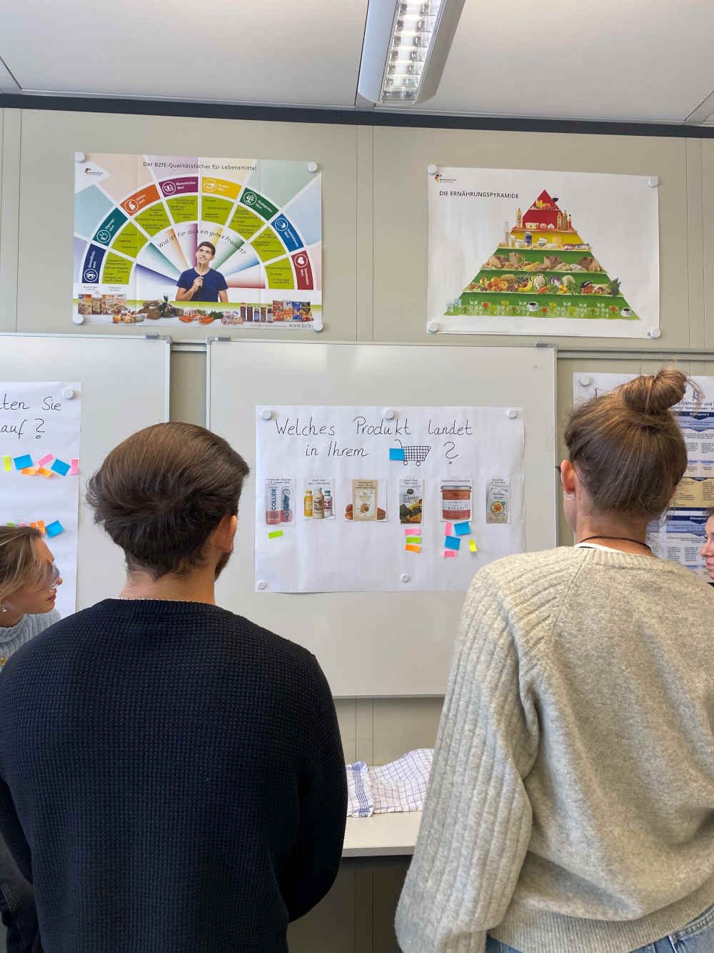 Zwei Personen sind von hinten zu sehen und blicken auf ein Plakat.
