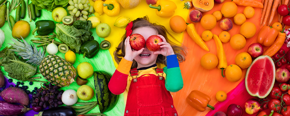 Mädchen vor einer bunten Gemüse- und Obstauswahl