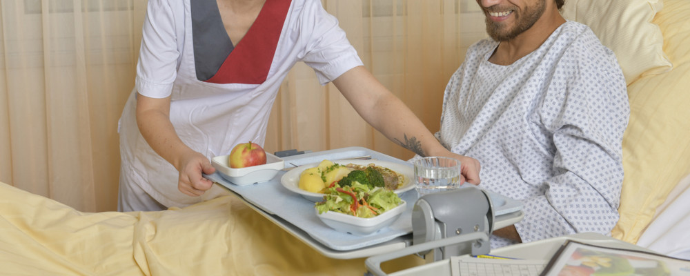 Patienten wird am Krankenhausbett Tablett mit Essen von Pflegekraft angereicht