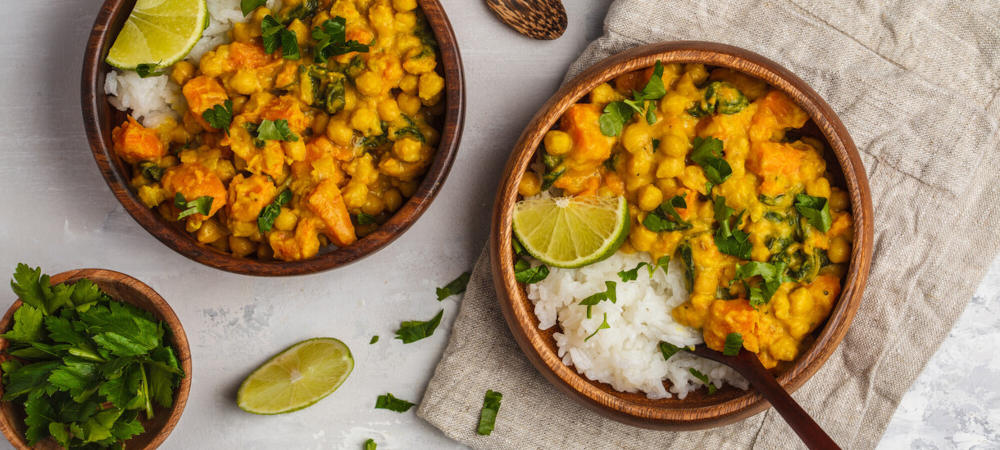 zwei Holzschalen gefüllt mit Kichererbsencurry und Reis als Beispiel für ein Gericht mit gut kombinierten pflanzlichen  Proteinen