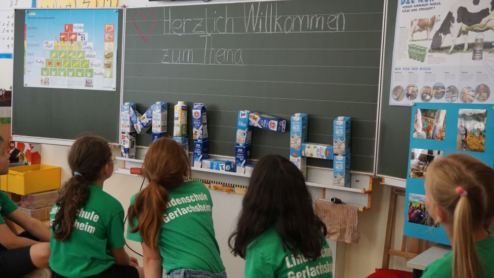 4 Kinder schauen auf die Tafel, an der das Wort Milch aus Milchkartons gebaut wurde
