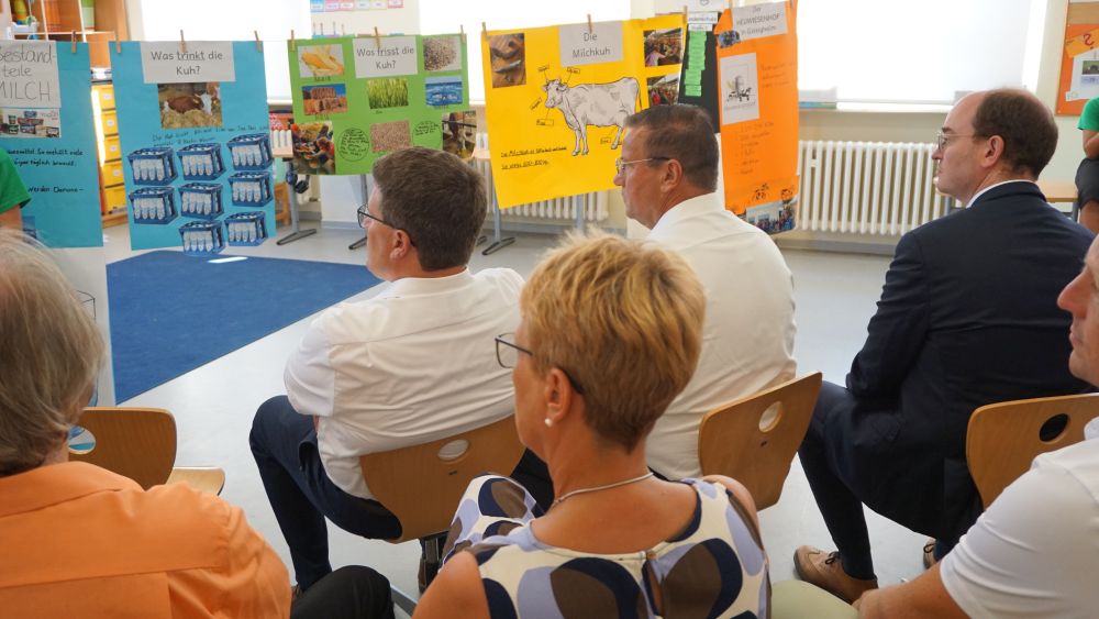 Erwachsene sitzen auf Kinderstühlen und schauen auf Poster zum Thema Milch