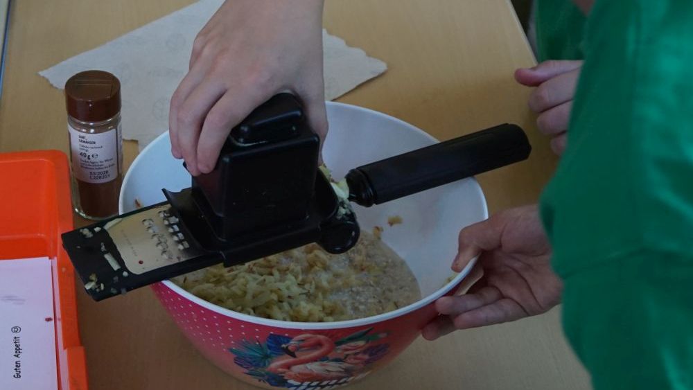 Eine Hand raspelt einen Apfel in eine Schüssel