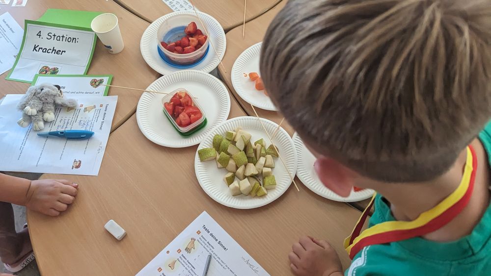 Ein Junge beugt sich über den Tisch, auf dem Teller mit verschiedenem Obst und Gemüse stehen